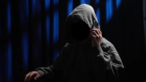 Anonymous hooded hacker talking on a smartphone in a dark room Stock Footage 318585017