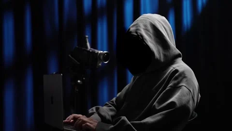 Anonymous hooded hacker typing on a laptop in a dark room Stock Footage 318297464