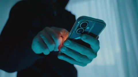 Anonymous hooded hacker typing on smartphone screen at night Stockbeeldmateriaal 339303152