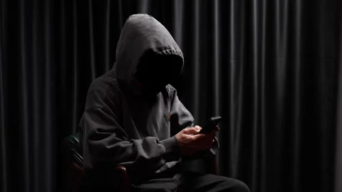 Anonymous hooded hacker using a smartphone Stock Footage 318297421