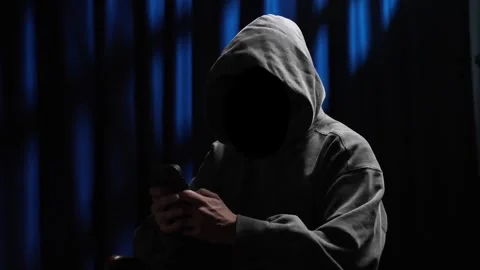 Anonymous hooded hacker using a smartphone Stock Footage 318585036