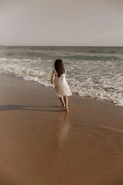 Anonymous kid running on sandy beach near wavy ocean Stock Photos