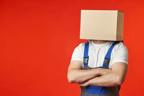 Anonymous loader in a work suit on a red background with a box on his head Stock Photos