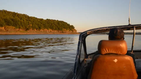 Anonymous man floats in old motorboat near shore with rock Stock Footage 67259727
