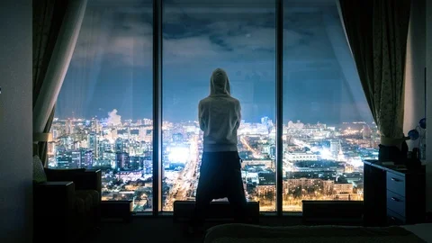 Anonymous man silhouette standing window dark room overlooking night city view Stock Footage 88384103