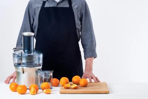 Anonymous man wearing an apron, preparing freshly made orange juice, using mo Stock Photos