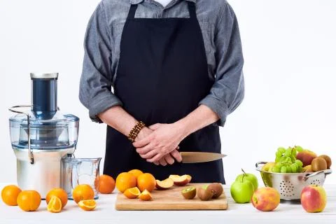 Anonymous man wearing an apron, preparing fresh fruit juice using modern elec Stock Photos
