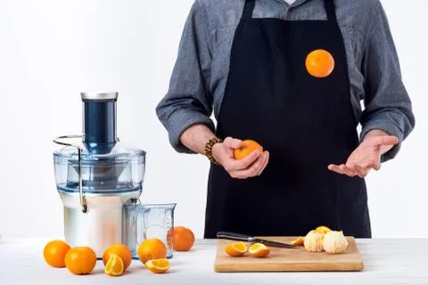 Anonymous man wearing an apron, preparing freshly made orange juice, using mo Stock Photos