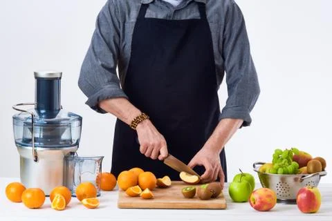 Anonymous man wearing an apron, preparing fresh fruit juice using modern elec Stock Photos