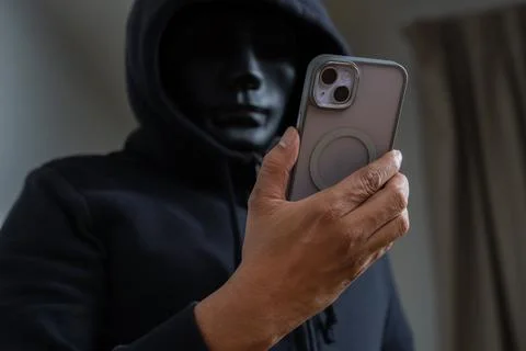 An anonymous masked hacker is using a smartphone to penetrate credit card f.. Stock Photos