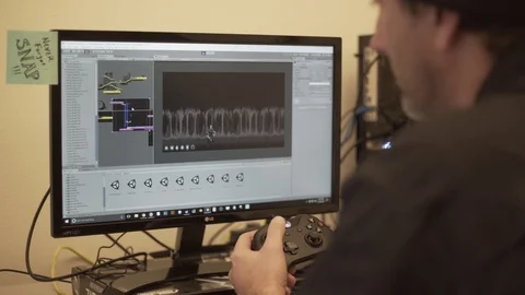 Anonymous Person Coding Game In Unity Pan Behind Shoulder Monitor Screen Stock Footage 88016390