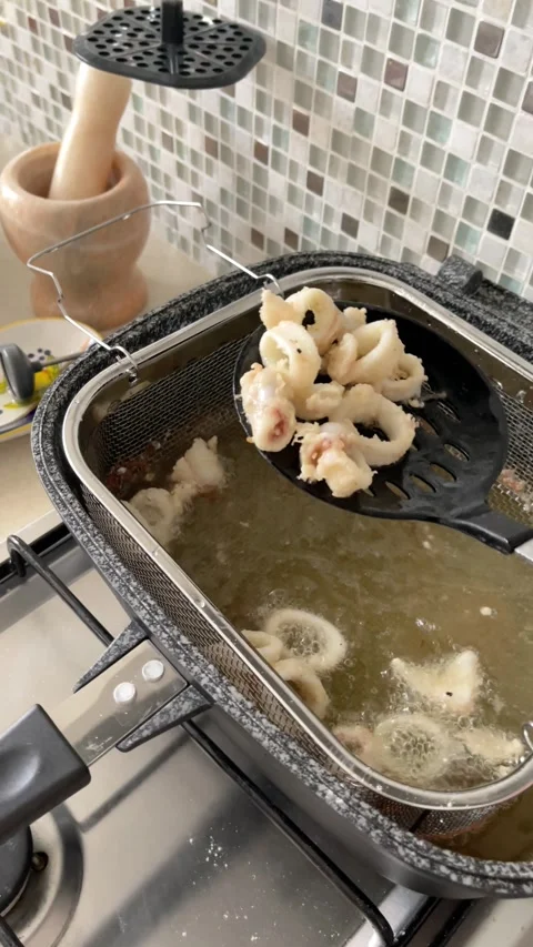Anonymous person removes rings of sliced, breaded, fried squid from hot frying Stock Footage 318463473