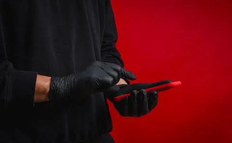 Anonymous scammer or hacker wearing black gloves using smartphone on red ba.. Stock Photos