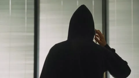Anonymous spy person or hacker with black hoodie talking on the phone indoors Stockbeeldmateriaal 329378915