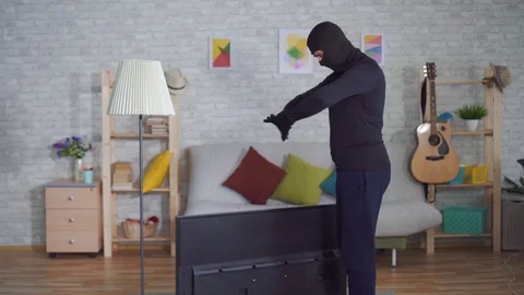 Anonymous thief in a Balaclava mask stealing TV in the house and experiencing Stock Footage 107110932