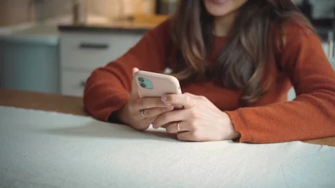 Anonymous woman using her smartphone in her home kitchen, highlighting mobile te Stock Footage 346321417