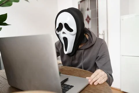 Anonymus person with ghost mask working with laptop. Halloween work concept Stock Photos