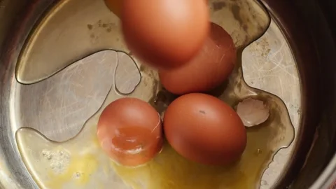 Another raw brown chicken egg falls into a metal pot from above, landing am.. Stock Footage 344112413