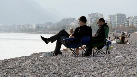 Antalya, Turkey - CIRCA 2022: Two local men sit in folding chairs on seashore on Stock Footage 227242640