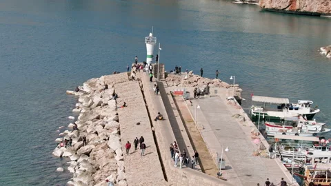 Antalya, Turkey - CIRCA 2023: Lighthouse on edge of spit in bay. Tourists walk Stock Footage 234935339