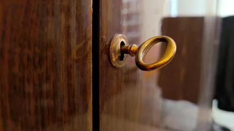 Antique brass key inserted into a keyhole on a classic dark wooden cabinet door. Stock Photos