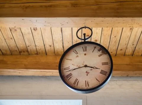 An antique clock with a large dial hangs on a wooden ceiling. Stock Photos