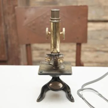 Antique microscope stands on a white table against the wooden wall of an old Stock Photos