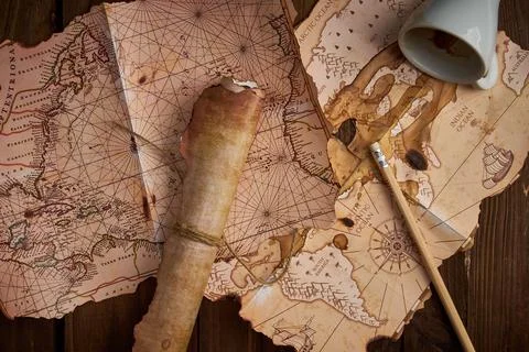 Antique parchment scroll with old maps and a spilled coffee cup on a wooden tabl Stockfoto's