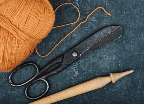 Antique rusty tailor scissors, tangle of orange color woolen yarn and spindle Stock Photos