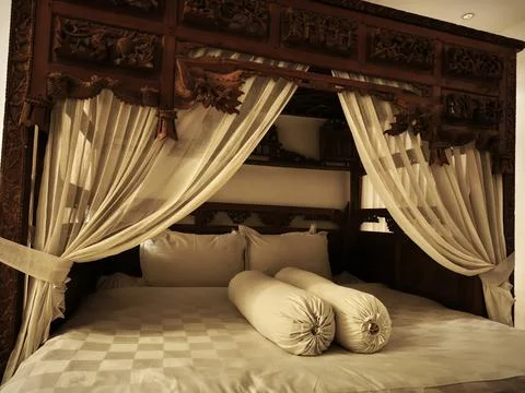 Antique teak canopy bed draped with sheer curtains in a hotel room Stock Photos
