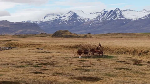 Antique wheel rake abandoned in field surrounded by snowy mountains Stock Footage 337961599