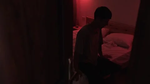 Anxious man sitting alone in a dark bedroom, nervously shaking his leg and Video stock 347301760