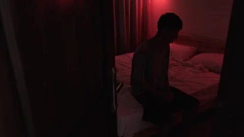 Anxious man sitting on a bed as tension builds, gripping his hands and moving Vidéo 347299562