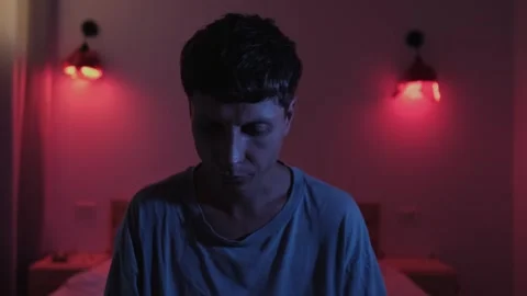 Anxious man sitting on his bed and looking around in confusion, struggling with Vídeos de archivo 347300944
