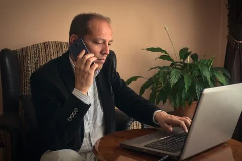 Anxious senior man phoning while working with his laptop at home Stock Photos