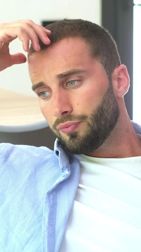 Anxious young man with a beard and blue eyes sitting alone, feeling stressed Vídeos de archivo 345124193
