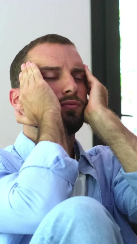 Anxious young man sitting alone at home, suffering from a severe headache Stock Footage 344781944