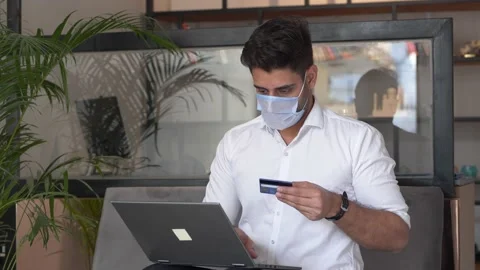 Anxious young man wearing protective face mask making online payment. Stockbeeldmateriaal 146301236