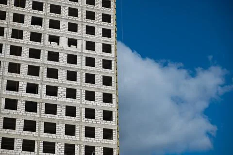 Apartment building under construction with empty windows against blue sky and Stock Photos