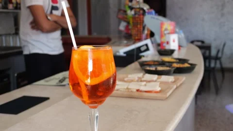 Aperol spritz and bar snacks resting on wooden counter with bartending prof.. Stock Footage 314886883