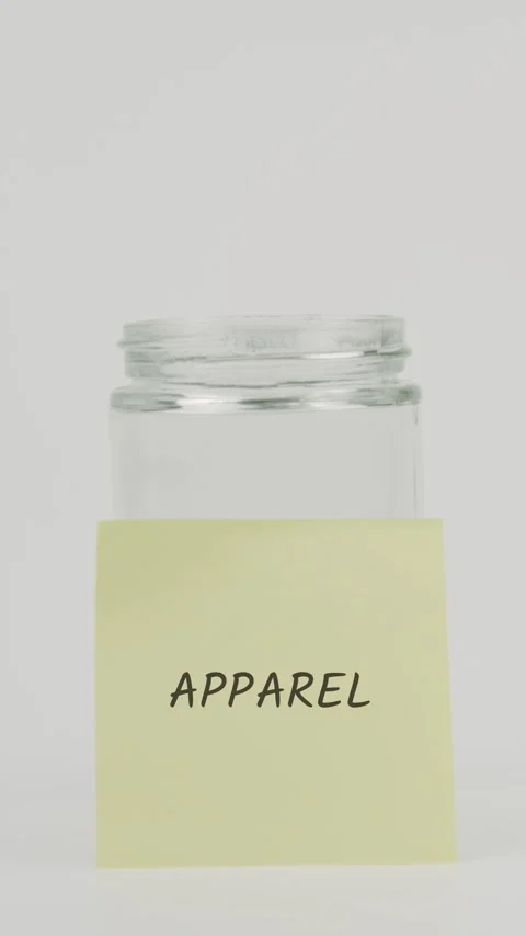 Apparel text or word on yellow sticky note attached to glass jar with hand Stock Footage 311677436