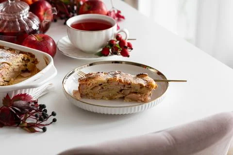 Appealing slice of apple pie with hot tea served on a white table surrounde.. Stock Photos