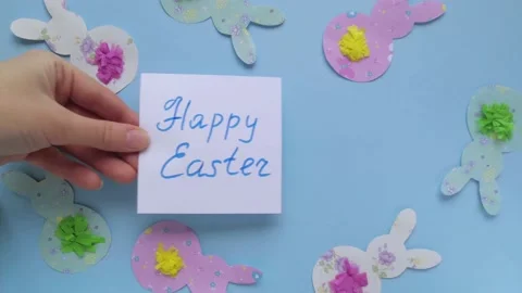 Appear note with words Happy Easter on blue background with rabbits and bunn Stock Footage 147357856