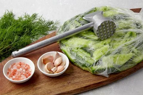 Appetizer Broken salted cucumbers in a plastic bag on a wooden cutting board  Stock Photos