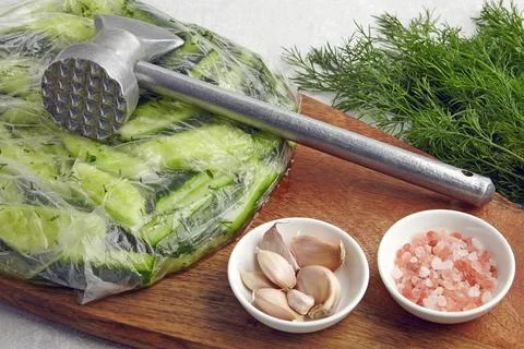 Appetizer Broken salted cucumbers in a plastic bag on a wooden cutting board  Stock Photos