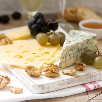 Appetizers of various types of cheese, grapes, nuts and honey, served with wh Stock Photos