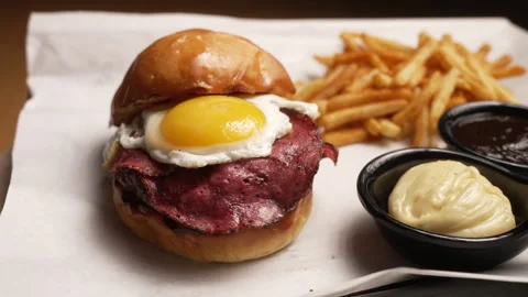 Appetizing burger with bacon, a fried egg, and french fries served on a platter 動画素材 333532106