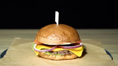 Appetizing burger with cutlet, lettuce, tomato, onion served on pieces of paper. Stock Footage 113605025