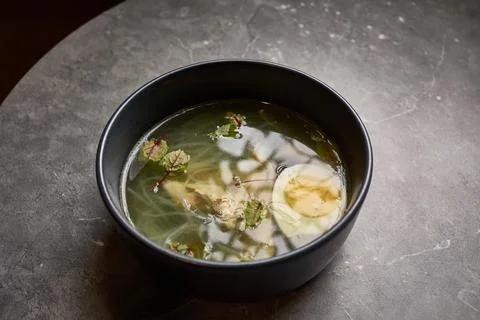 Appetizing clear soup with egg, herbs, noodles in bowl on gray marble table.. Stock Photos