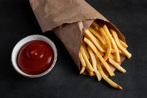 Appetizing crispy fries in an eco-friendly paper bag on black background. H.. Stock Photos